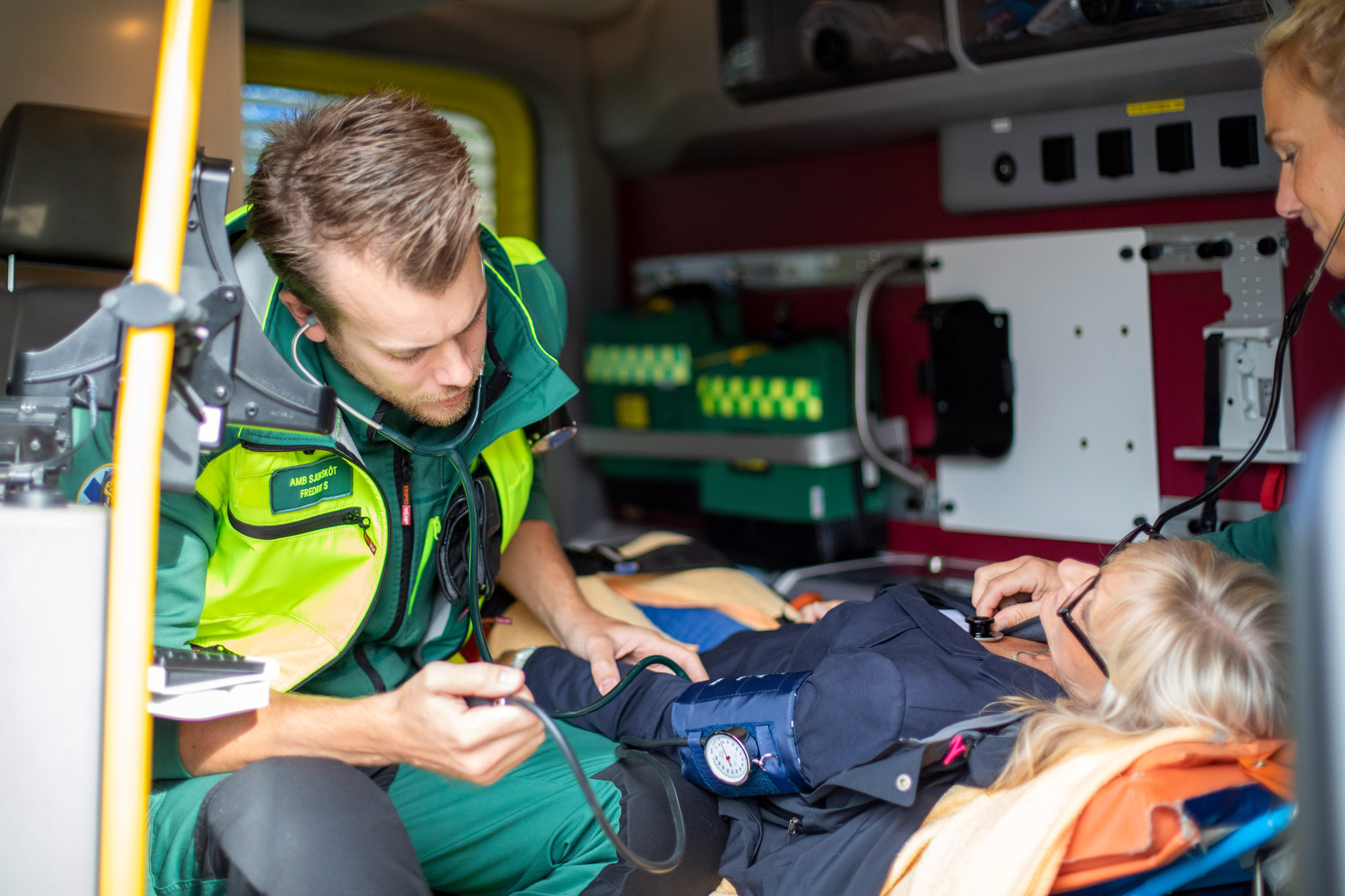 Medarbetare tar blodtryck och kollegan lyssnar på lungorna på patienten bak i ambulansen.