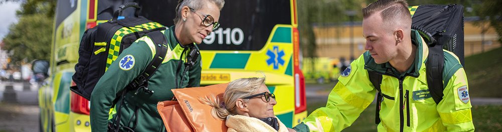 Ambulanssjukvårdare lägger handen på patientens axel som ligger på båren,